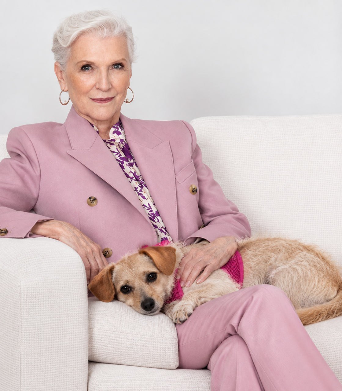 Maye Musk sitting on a cream sofa with Cali resting beside her